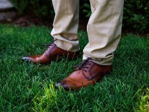 Close-up sequence of brown leather dress shoes walking on lush green grass.