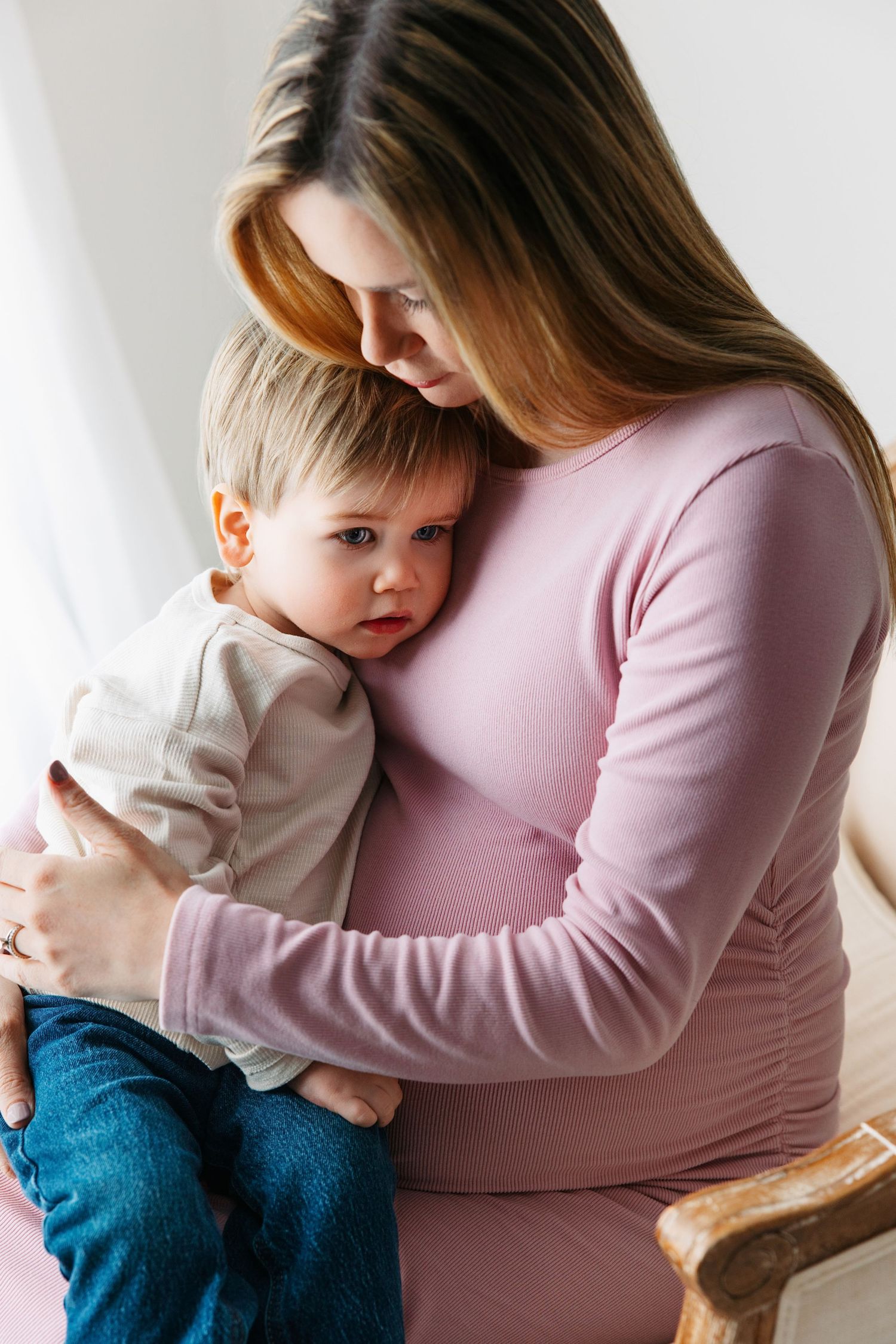 Mom cuddling toddler son in a light colored shirt, during maternity photoshoot in Pleasant View.