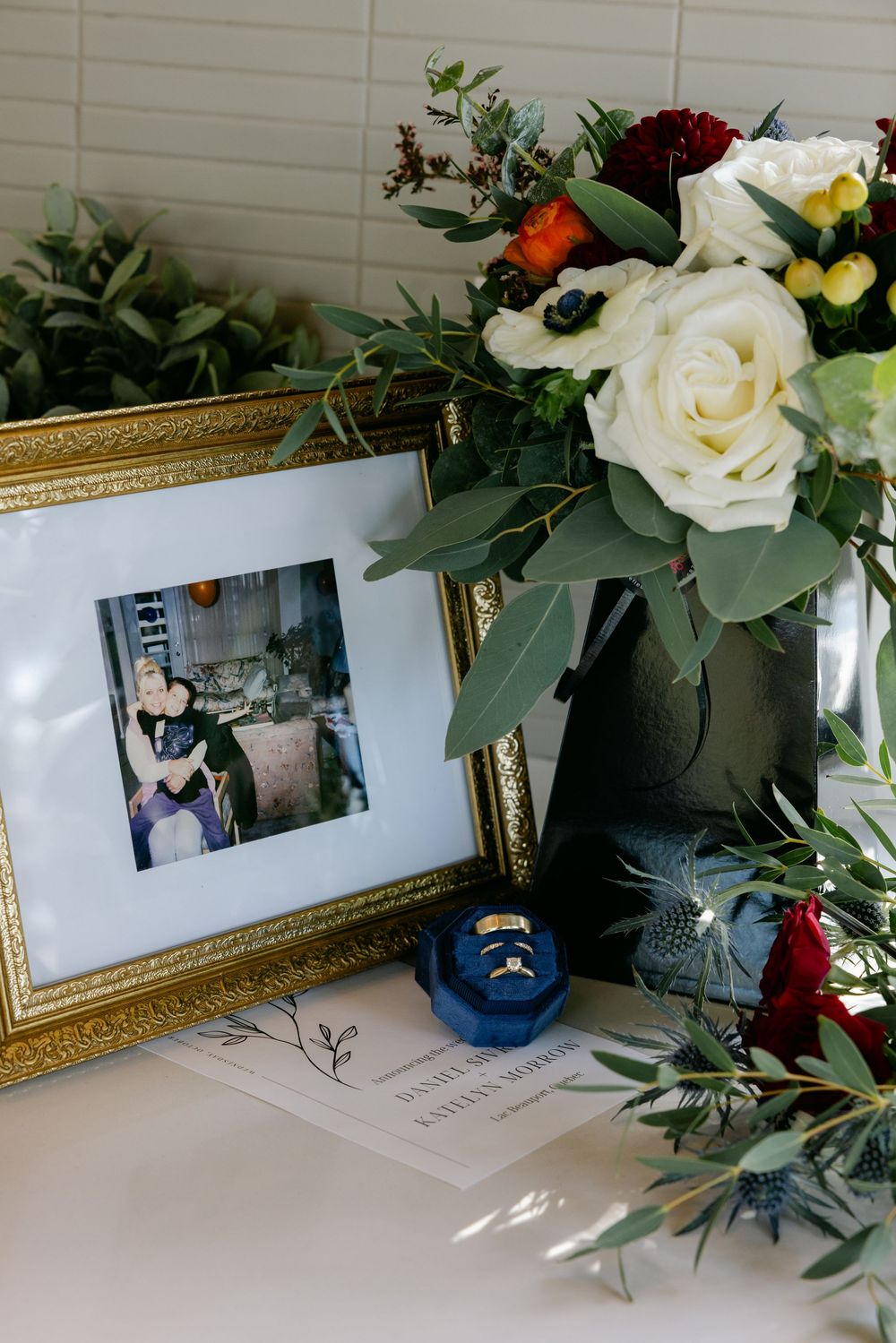 Elegant floral arrangement with white roses next to a framed photograph and blue ring box.
