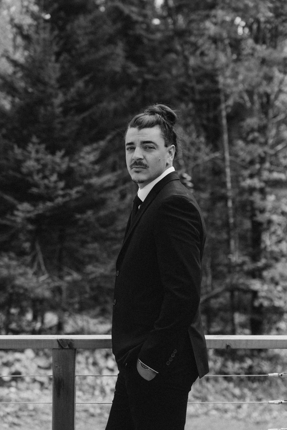 A black and white portrait in a forest setting with a wooden railing.