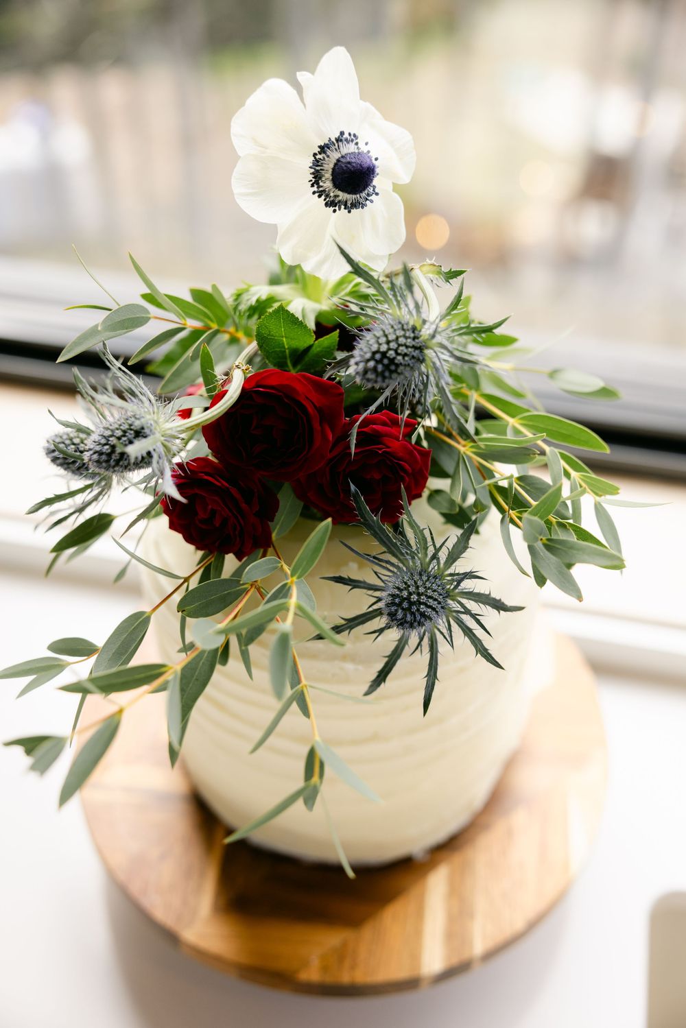 White ceramic vases with red and white anemone flowers and eucalyptus arranged on wooden coasters.