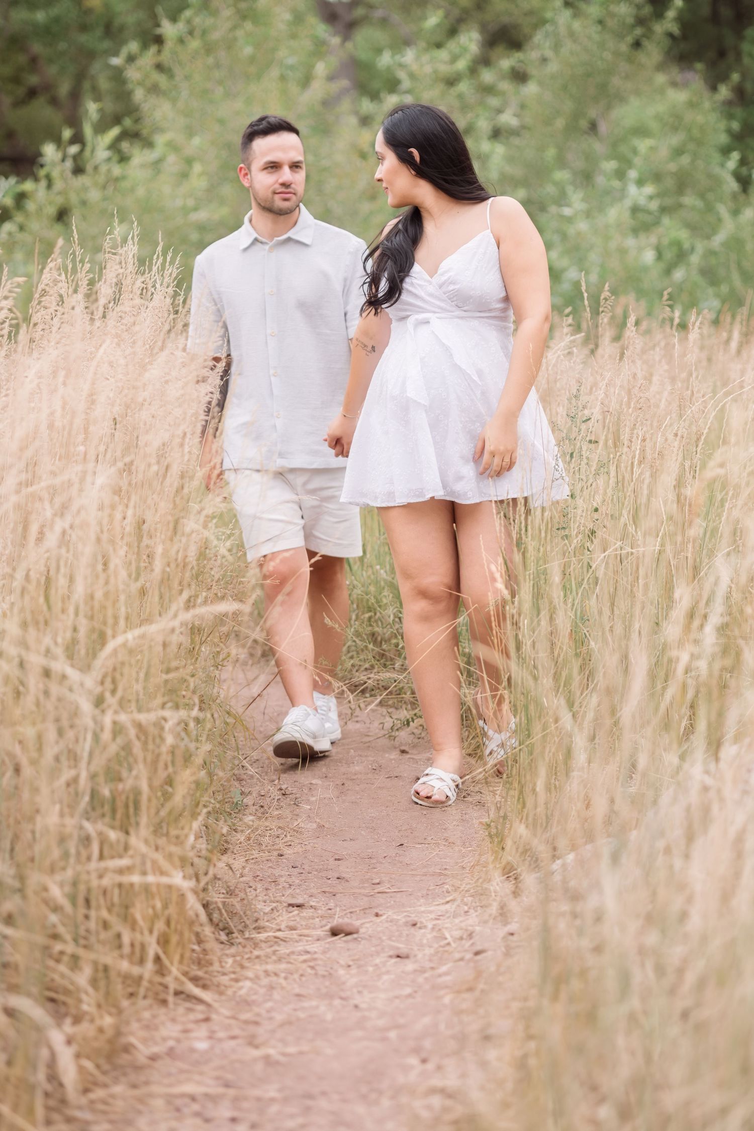 A couple walking together on a dirt path through tall golden grass on a summer afternoon.