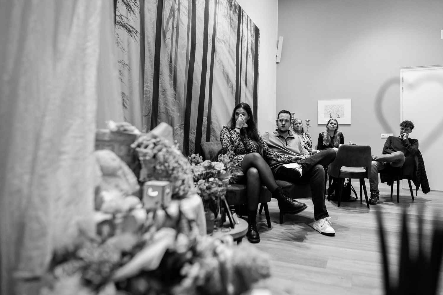 People seated in a room with forest-themed wall murals and decorative floral arrangements.