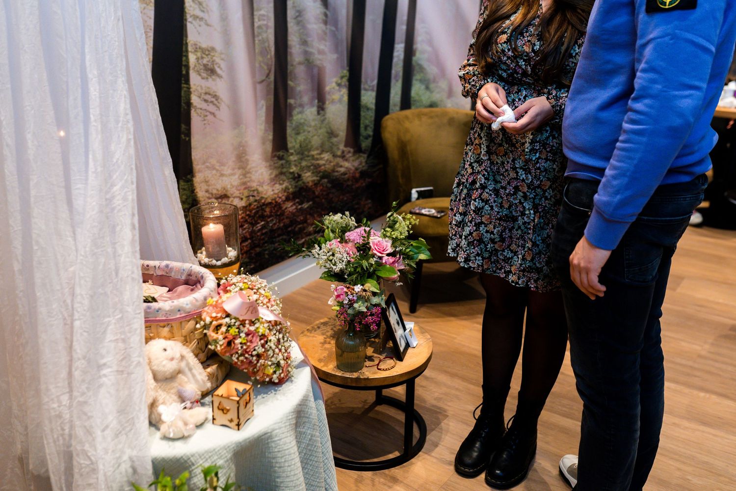 Guests examining decorative food and flower arrangements on a table with forest-themed backdrop.