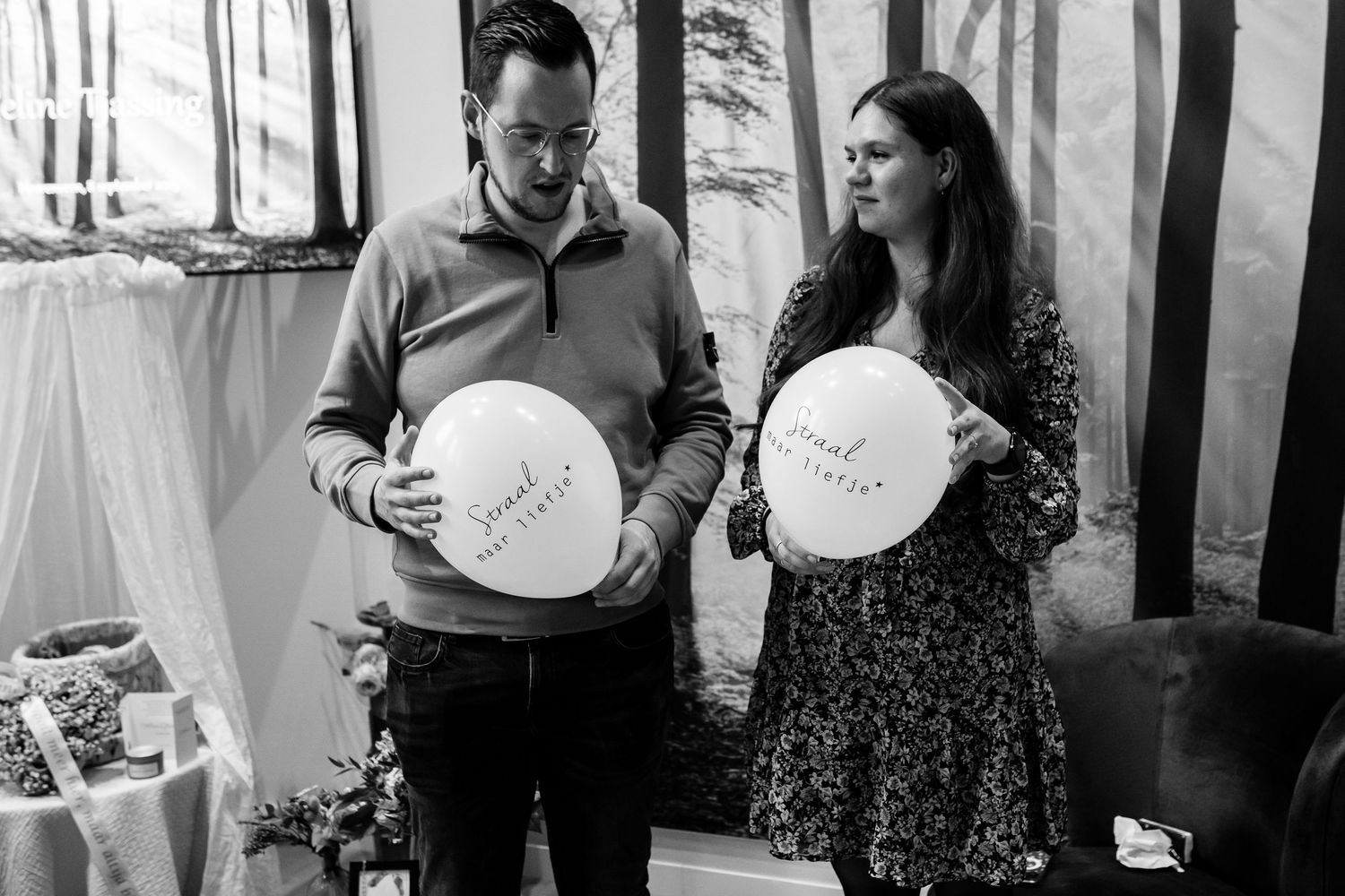 Two people holding white balloons against a forest-themed backdrop at an event.