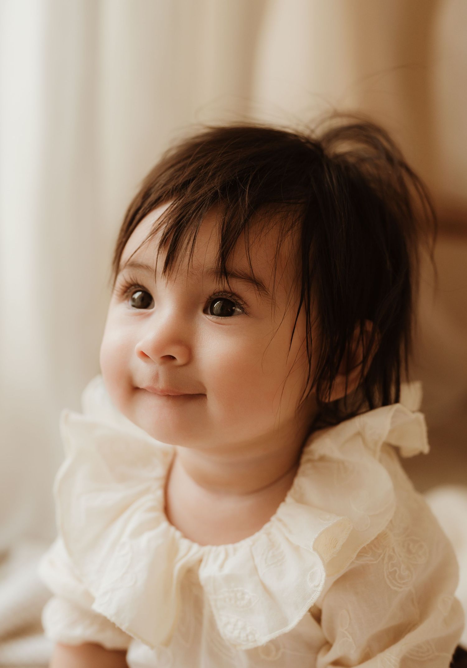 A small baby wrapped in a cozy white knit sweater lies on cream-colored fabric while a gentle hand rests on their head.