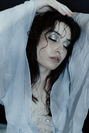 Artistic portrait series showing a person with dark hair against white fabric in dramatic poses with pearl necklace details.