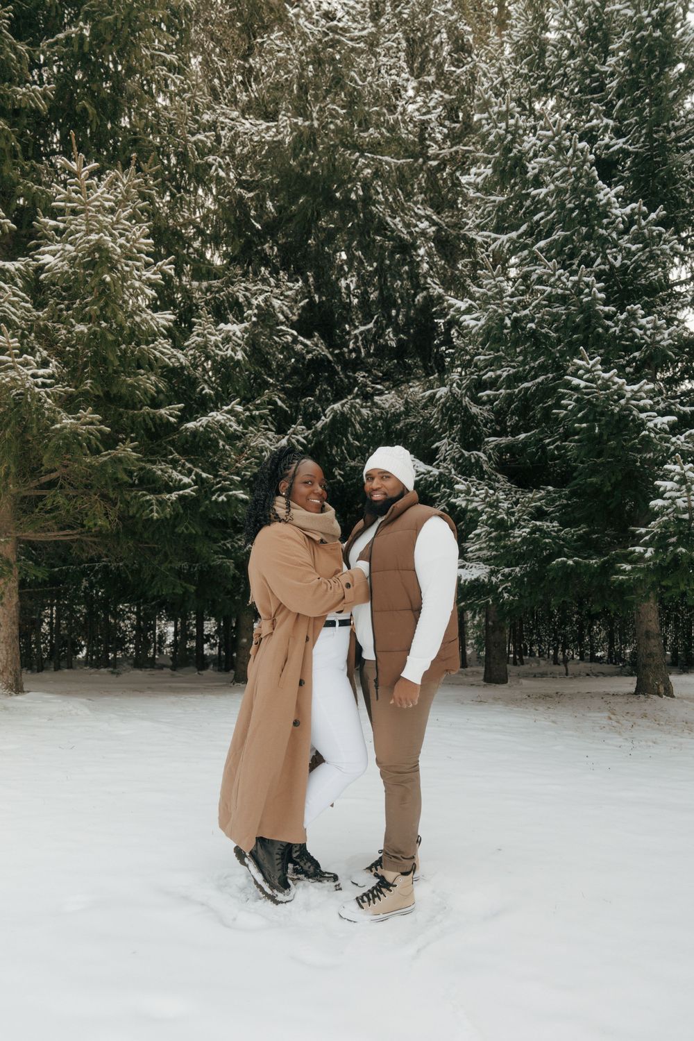 A couple shares romantic moments in a snowy forest setting while wearing winter coats.