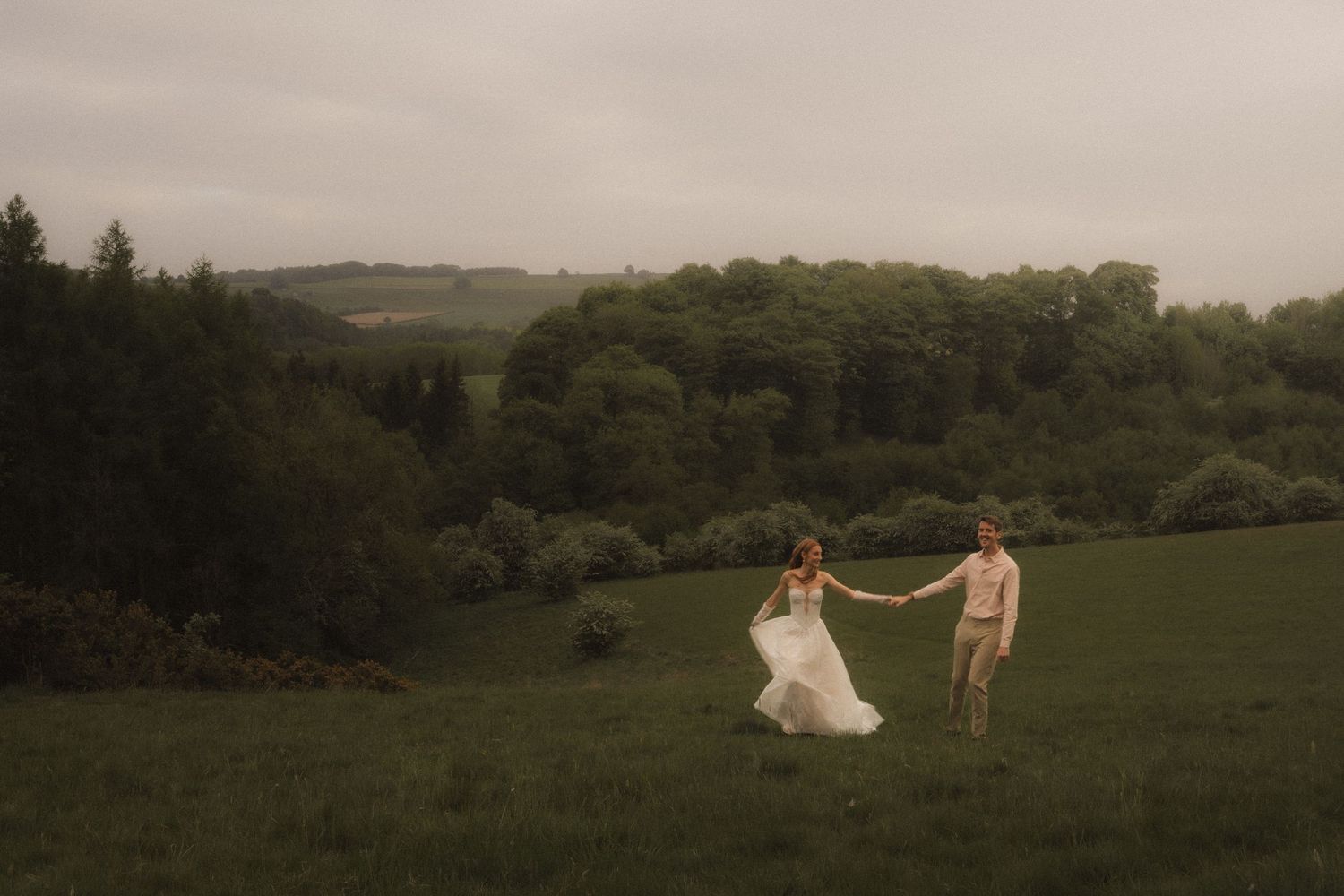Couple in wedding attire stands near a lake with dramatic mountains and moody skies in the Scottish Highlands.