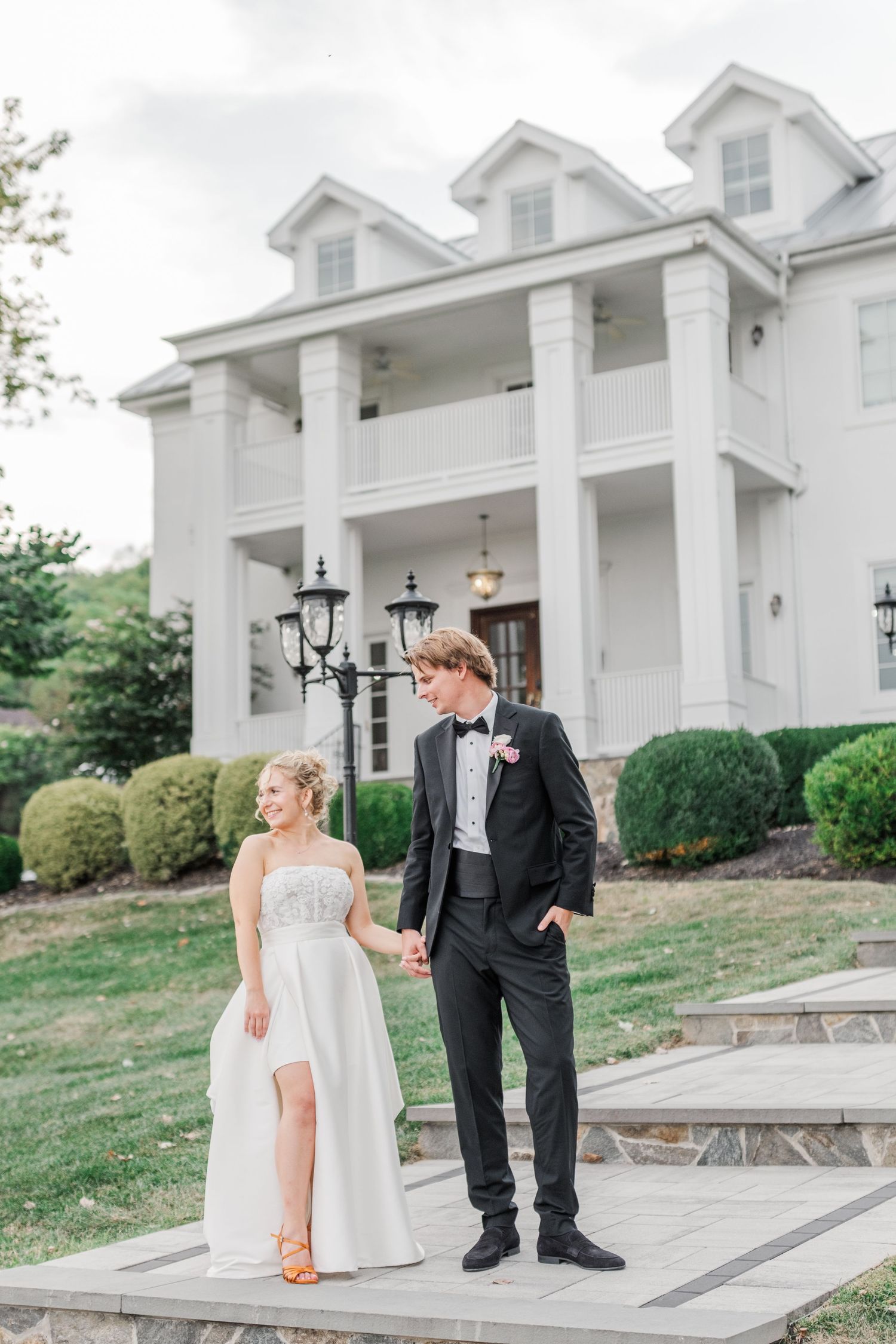 A wedding couple standing outside a grand white colonial-style mansion with columns.