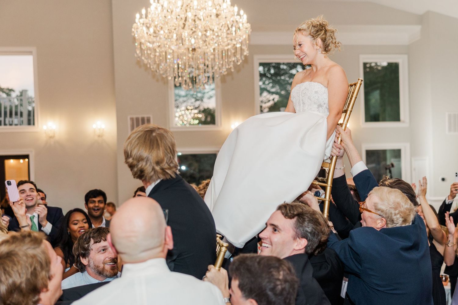 Wedding reception guests celebrate with raised arms and joyful expressions on the dance floor.