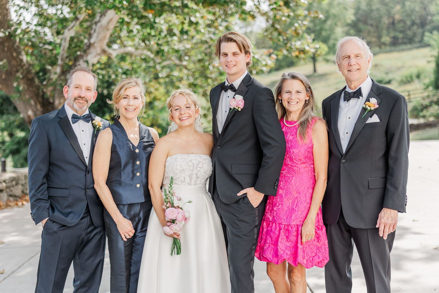 Formal wedding party poses outdoors with a bride in white and guest in bright pink dress.