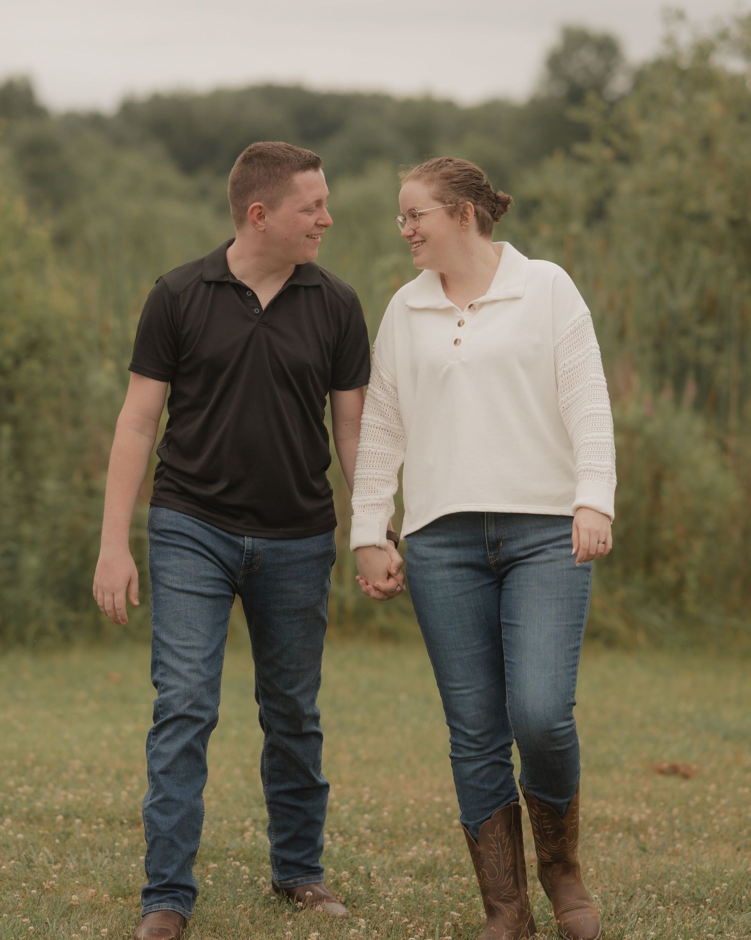 A couple holding hands while walking in a grassy field on a sunny day, shown from the waist down.