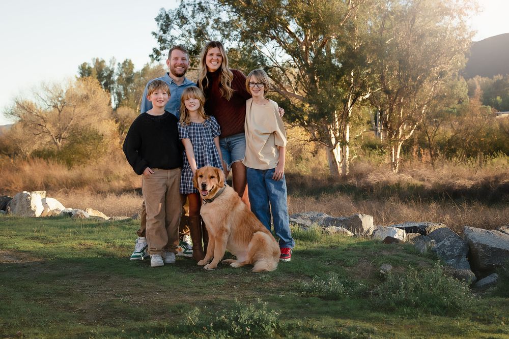 A group of people and their golden retriever dog pose together outdoors during golden hour at sunset.