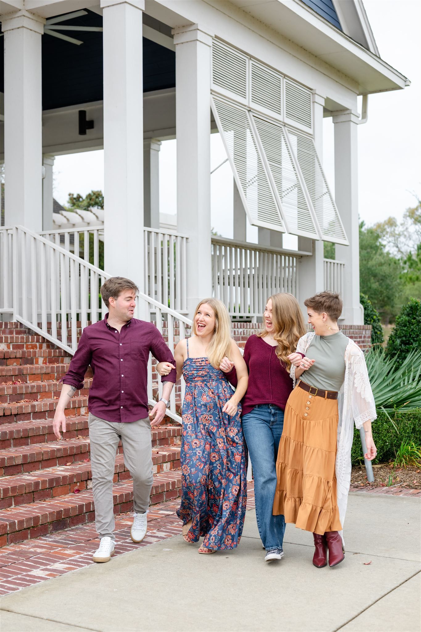 A group of sisters and brother laughs together on brick steps of a white-columned porch in Conroe, texas.