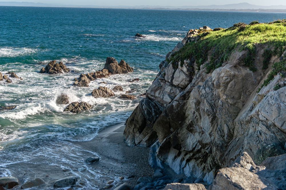 Rocky coastal cliffs meet crashing ocean waves under a clear blue sky in this stunning seaside landscape.