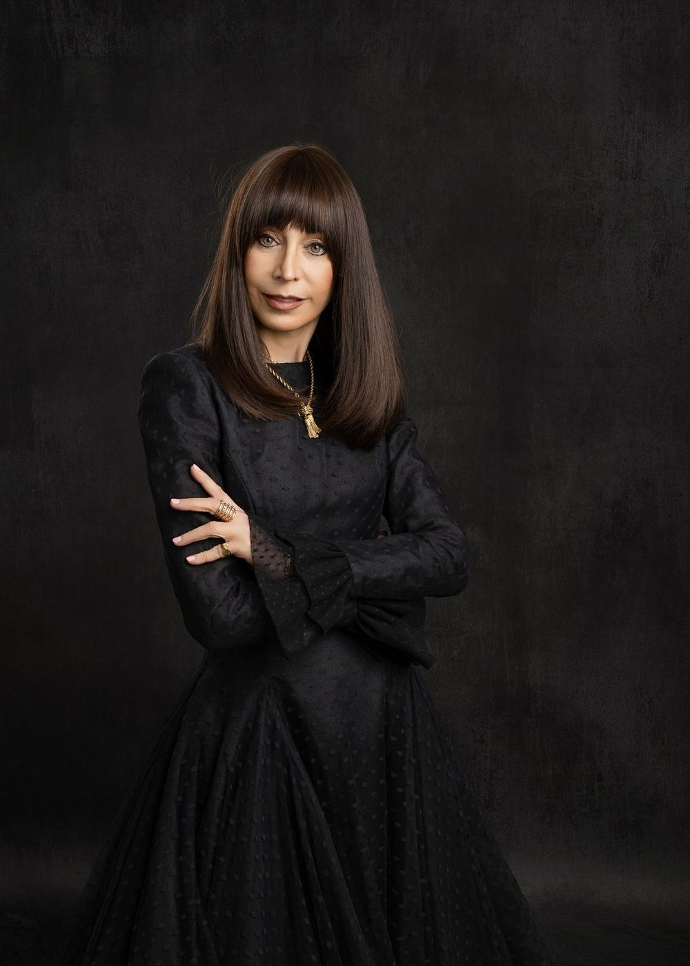 A figure in a black dress poses expressively against a dark background in a dramatic fashion portrait series.