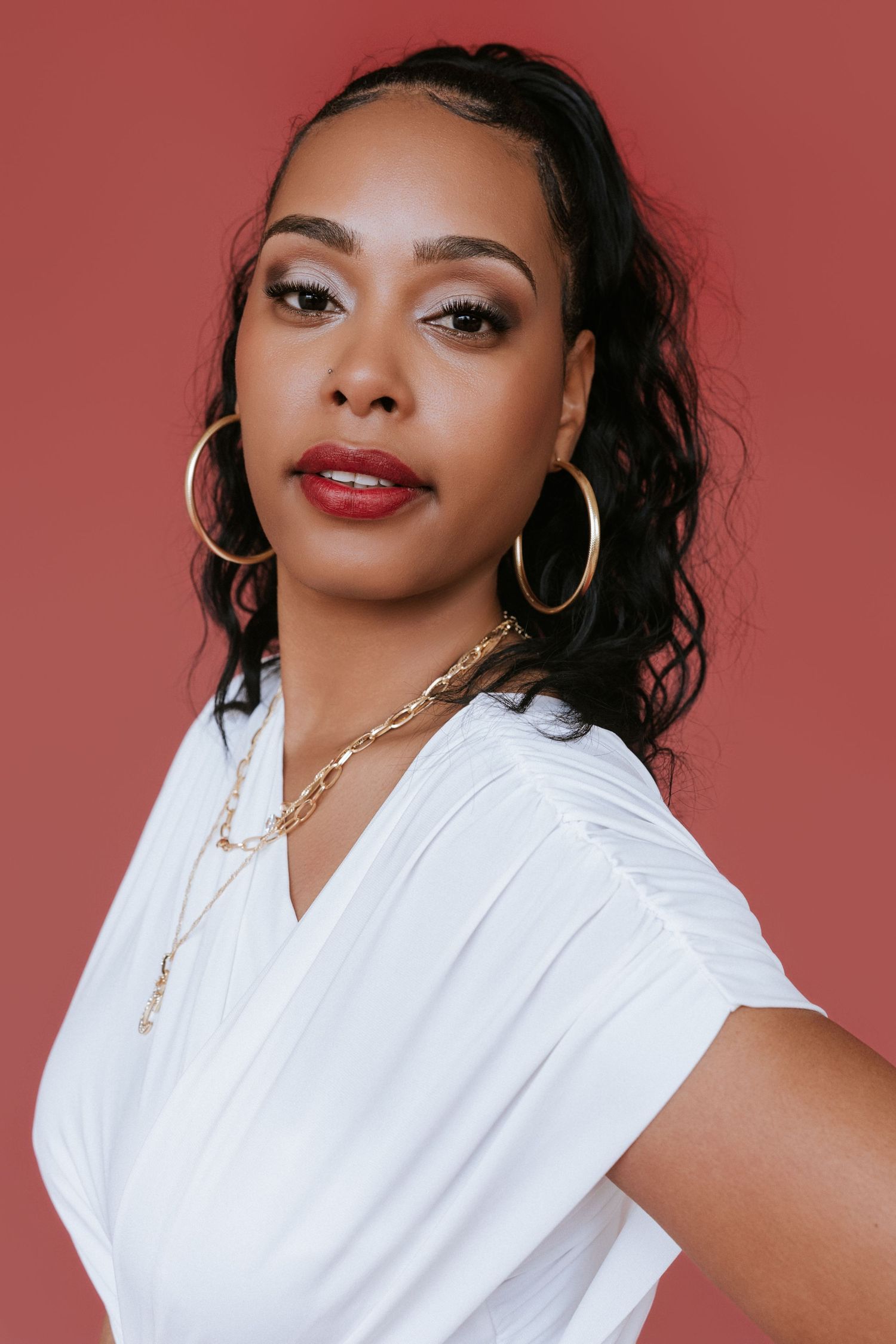 A series of four beauty portraits against a red background featuring gold hoop earrings and a crisp white top.