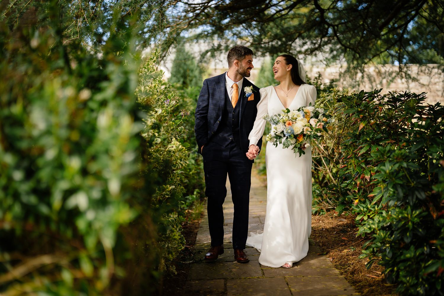 Romantic garden wedding scene with couple walking among green foliage and natural light. Ellingham Hall