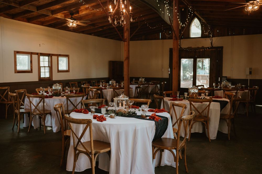 Rustic wedding reception venue with wooden cross-back chairs and white tablecloths set for celebration.