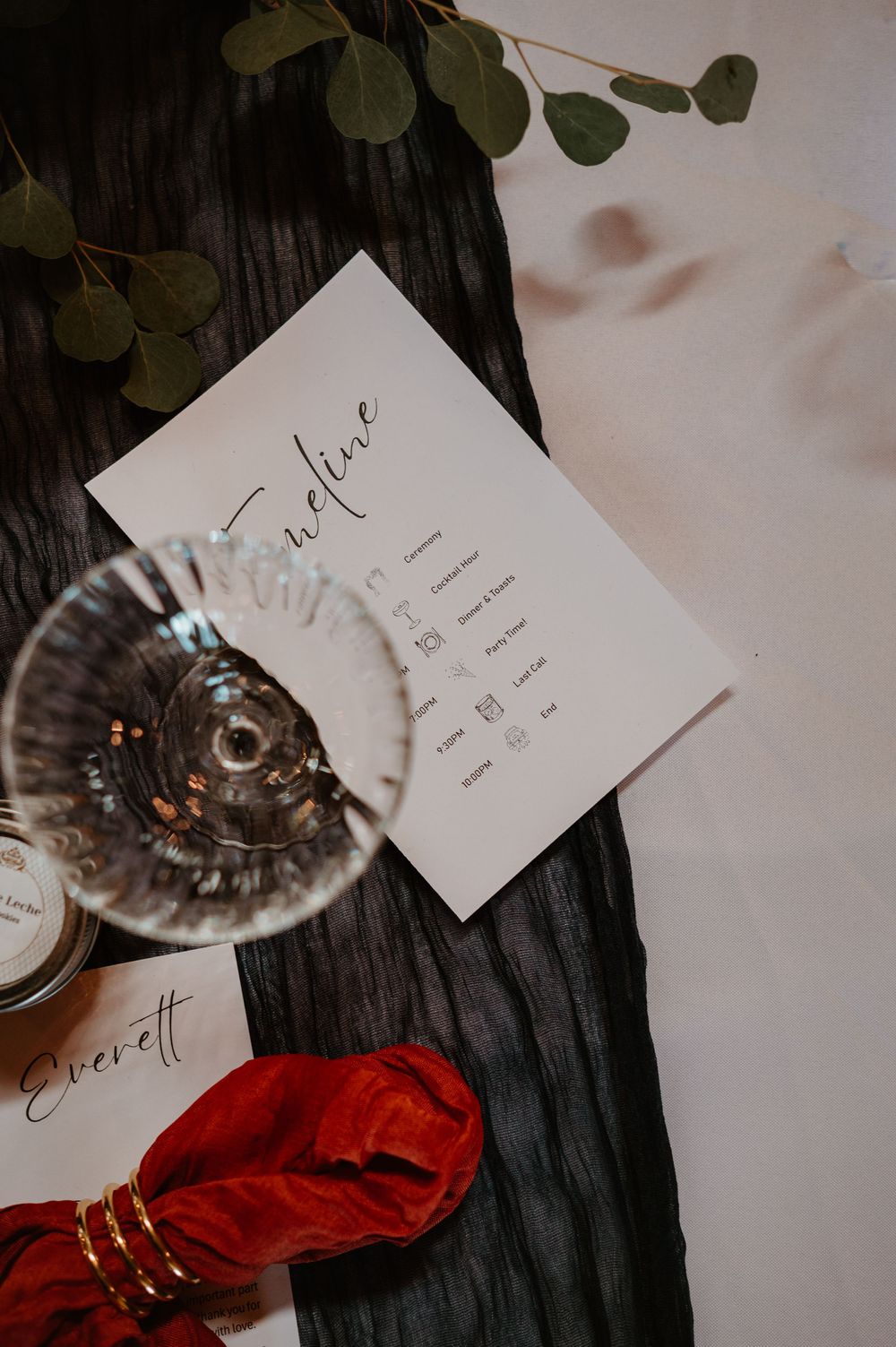 Wedding place cards and table settings with red napkins on a dark wooden surface.