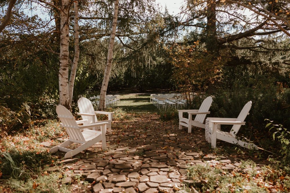 White Adirondack chairs arranged in a rustic outdoor setting among autumn trees.