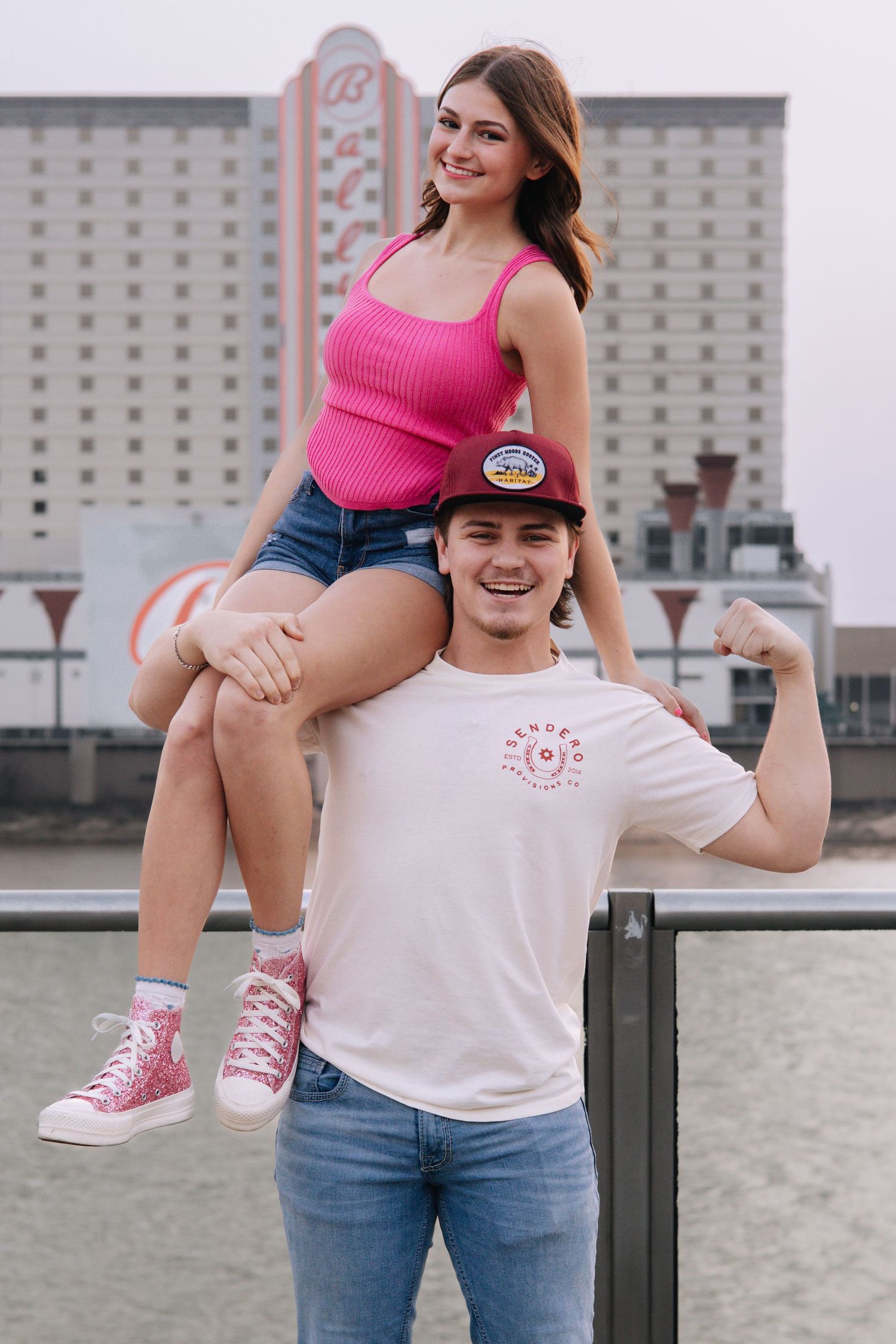 Playful maternity photos with pink tank top and casual denim against urban backdrop.
