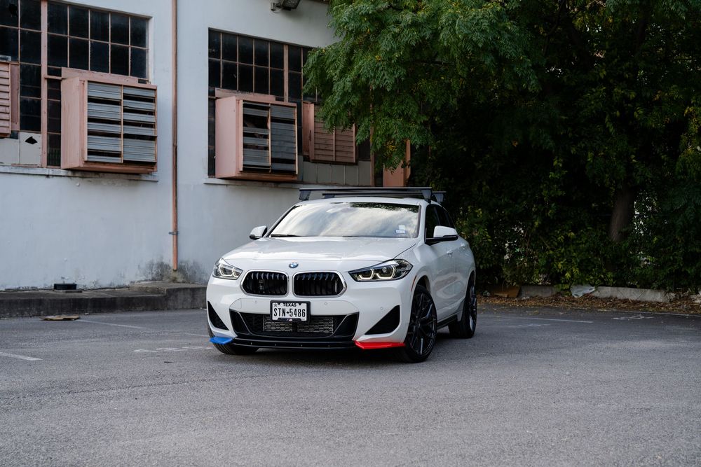A row of white BMW vehicles parked in a parking lot with trees visible in the background.