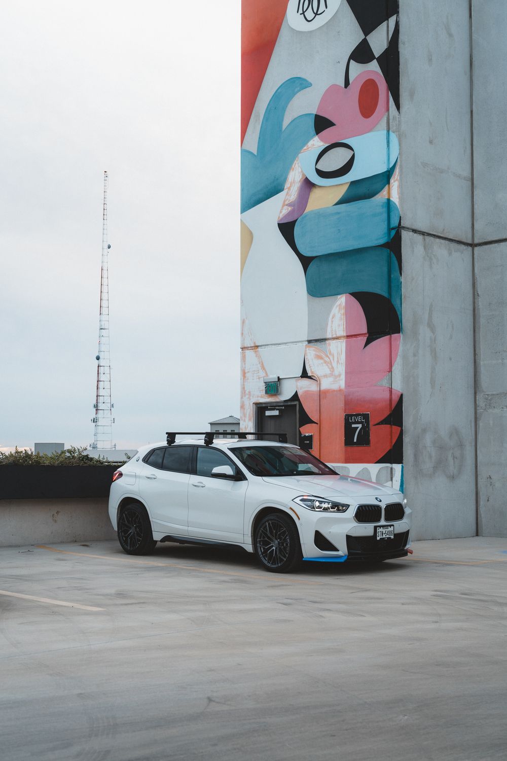 White BMW M4 sports car parked against a concrete wall with colorful modern art mural in an urban setting.