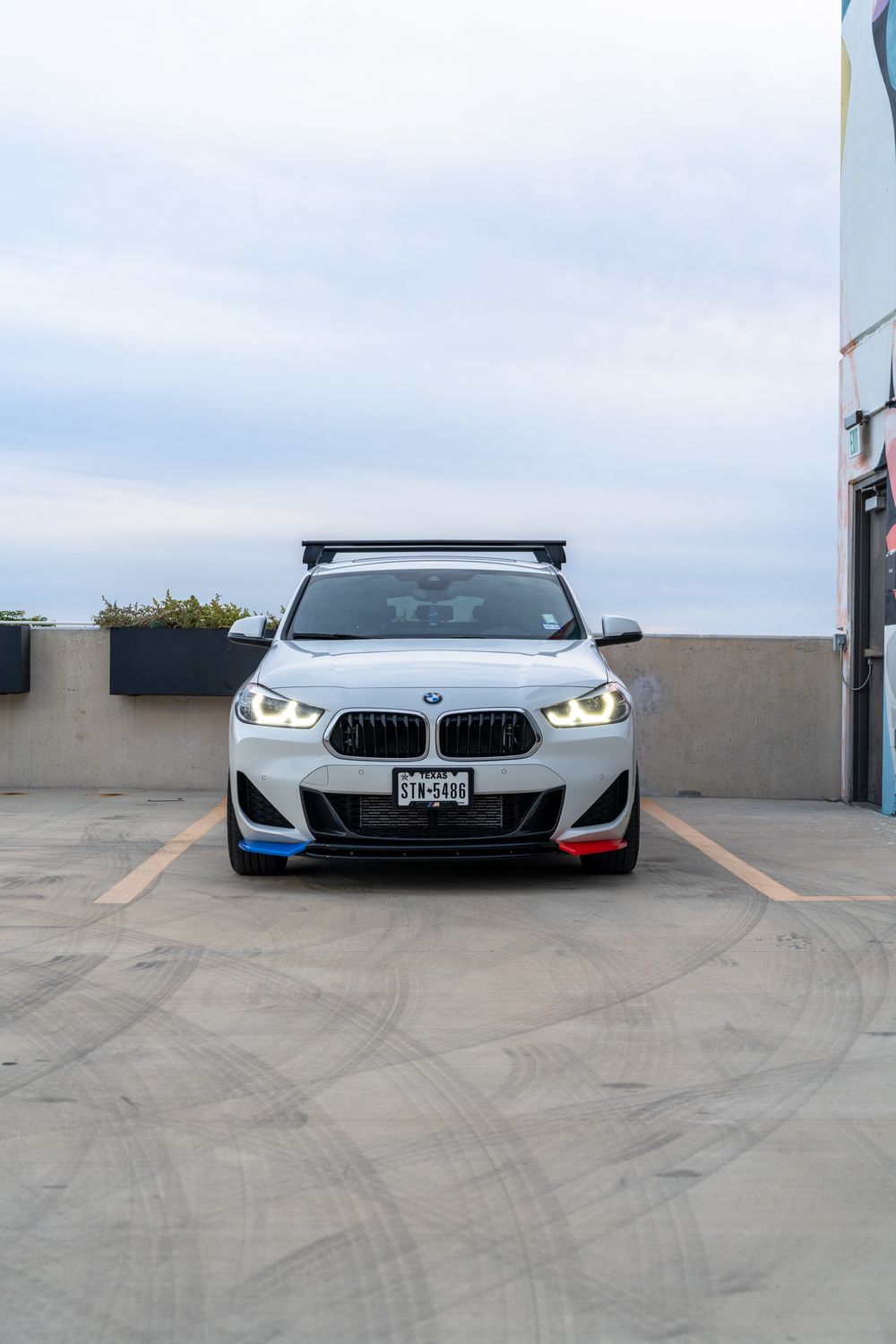 White BMW M235i Gran Coupe with illuminated headlights and M-colored accents parked in an empty parking lot.