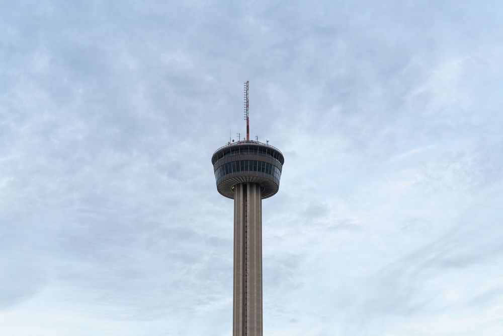 The Tower of the Americas rises into a cloudy sky in San Antonio, Texas, showcasing its distinctive observation deck.