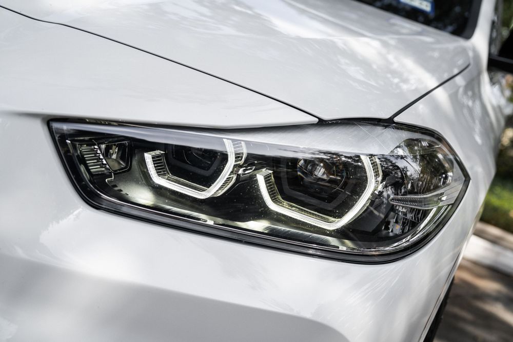 Modern LED headlight detail of a white BMW car featuring distinctive angular design and daytime running lights.