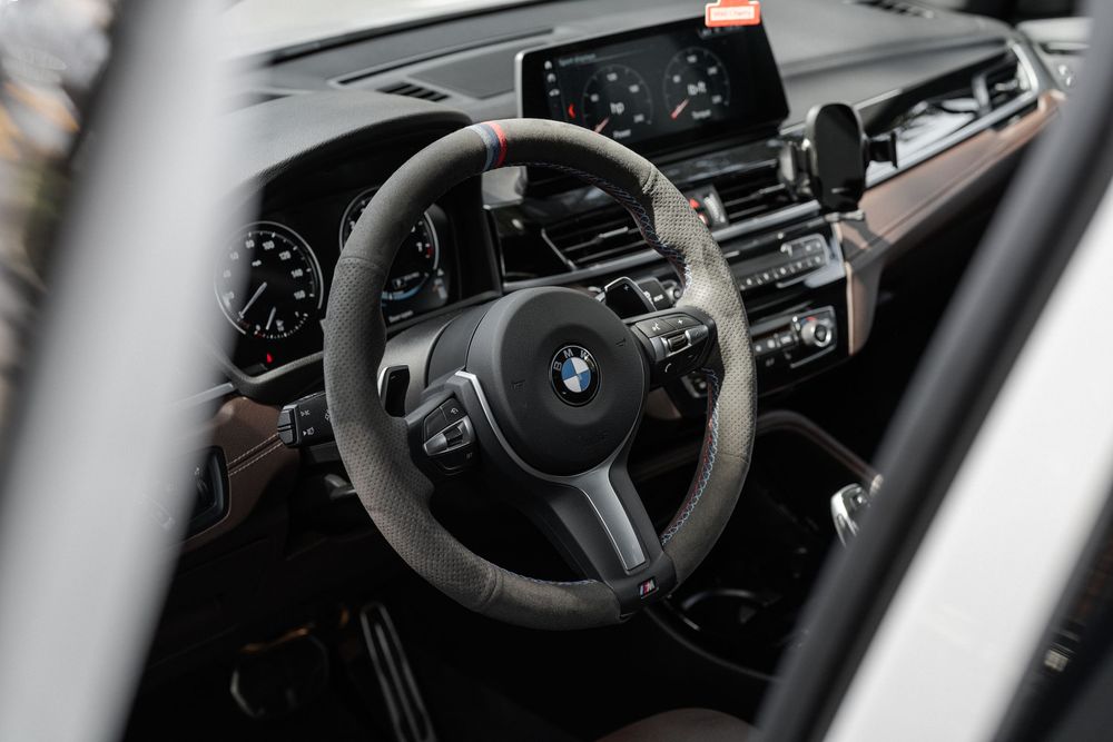 Interior view of a BMW vehicle showing the steering wheel, dashboard and modern cockpit controls in a luxury setting.