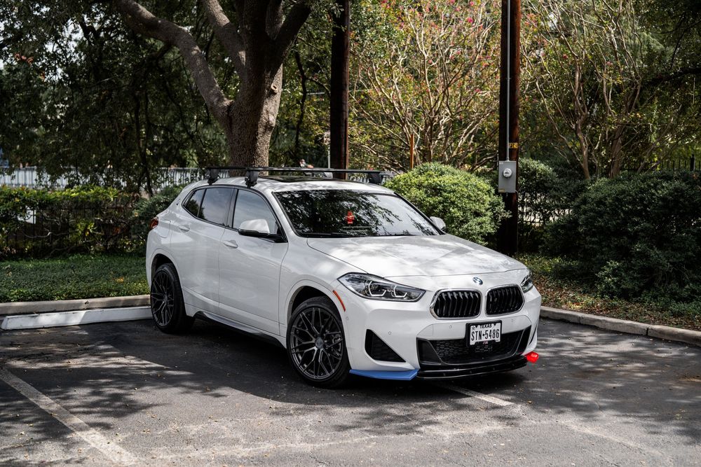 White BMW 2 Series Gran Coupe parked in a shaded outdoor spot with trees in the background.