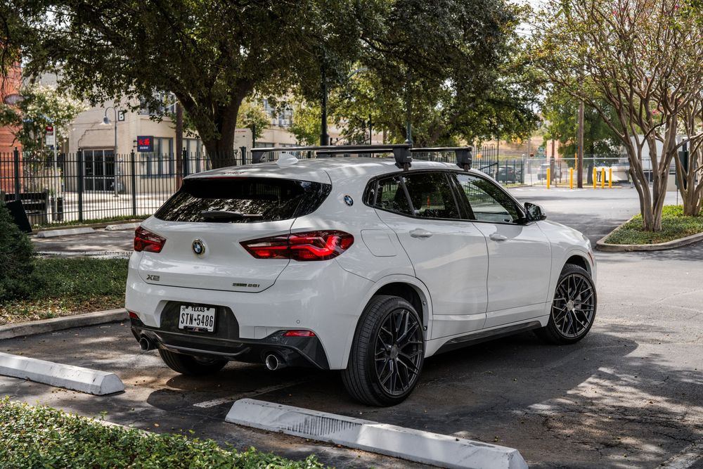 White BMW X2 crossover SUV parked on a tree-lined street with custom black wheels and sport styling package.