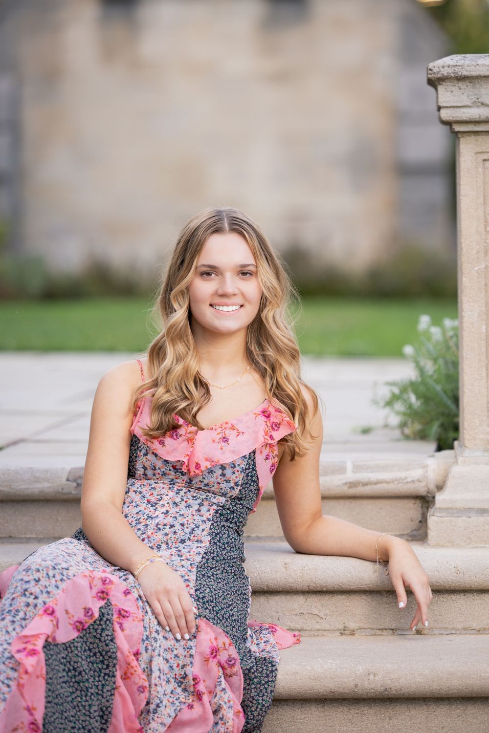 A person in a floral pink and gray dress sits on stone steps outdoors during a portrait session.