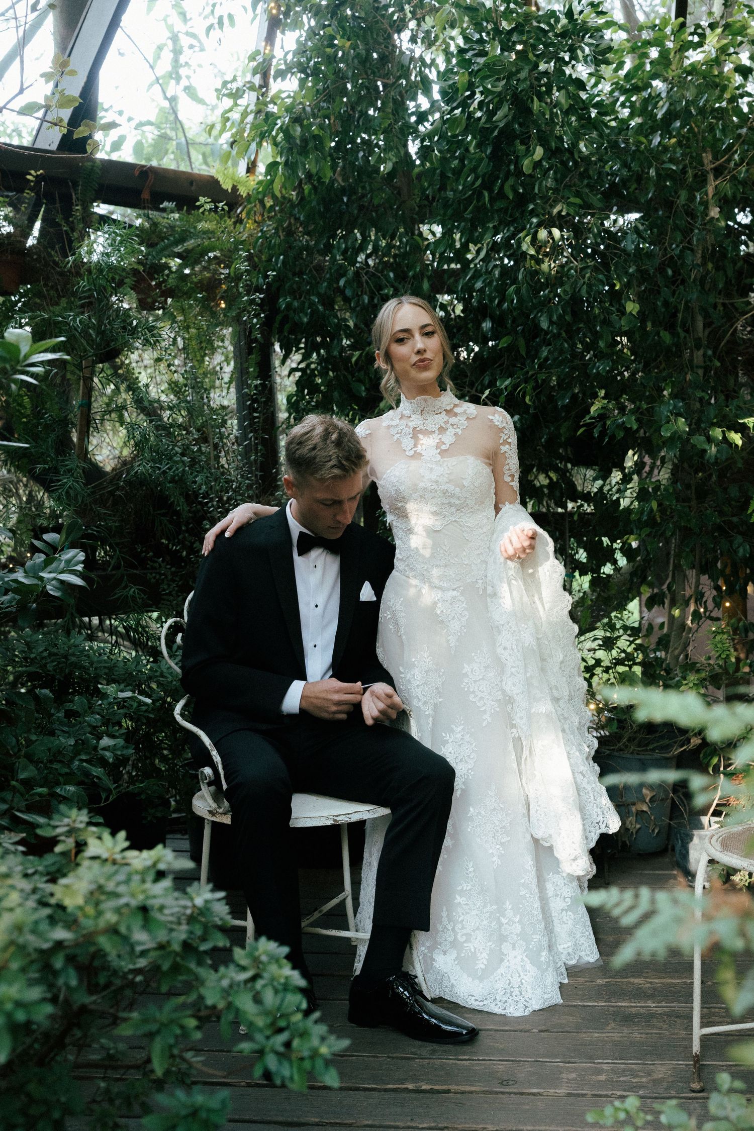 A couple in wedding attire shares a romantic moment together on a wooden deck surrounded by lush greenery in Fallbrook Twin Oaks venue