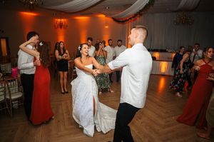 Wedding guests dance together on a wooden dance floor at an indoor reception with decorative white draping overhead.