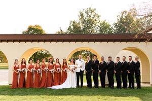 Wedding party members in red dresses and black suits pose together in front of a white building.