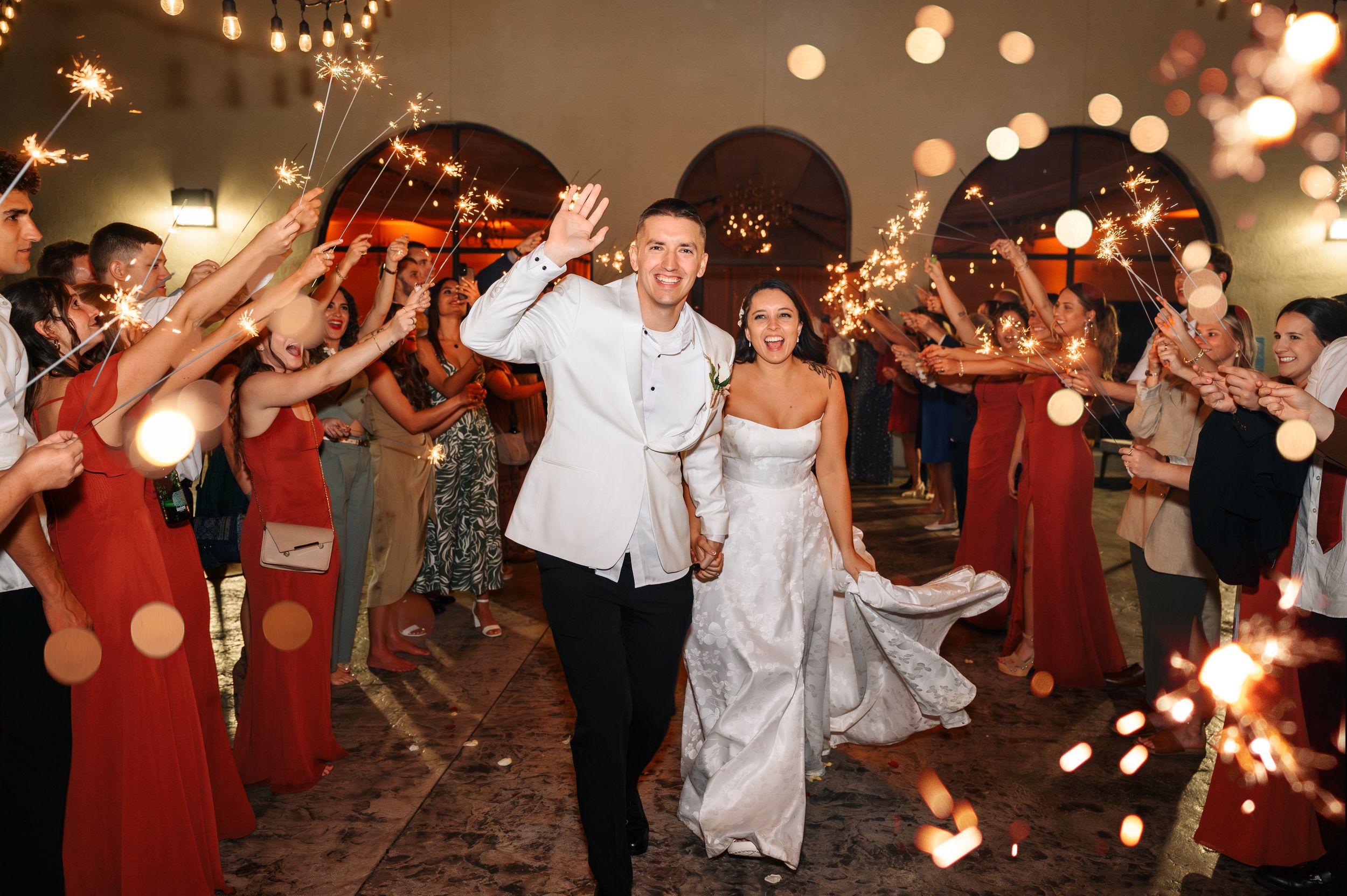 Wedding guests hold sparklers creating a magical tunnel of light for the newlyweds during an evening reception exit.