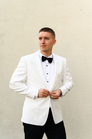 A person in a white dinner jacket and black bow tie adjusts their sleeves in a formal portrait series.