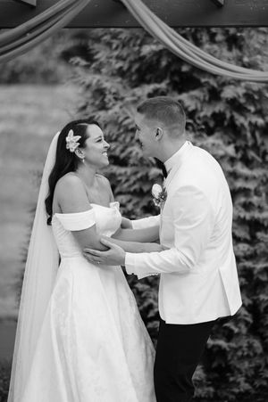 A bride and groom share a joyful moment during their black and white wedding ceremony under draped fabric outdoors.