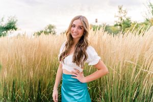 A person in a turquoise dress poses in a field of tall wheat grass during golden hour.