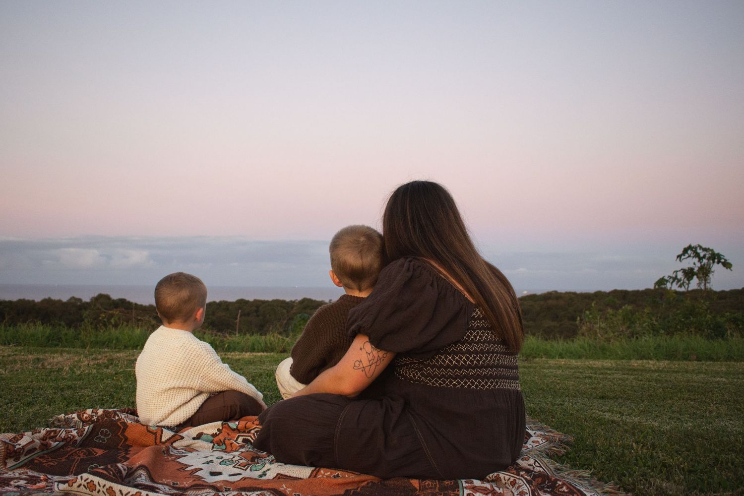Mum sitting at a lookout with her two young children at Sunset motherhood photoshoot at Whitebridge lookout Dudley beach Newcastle