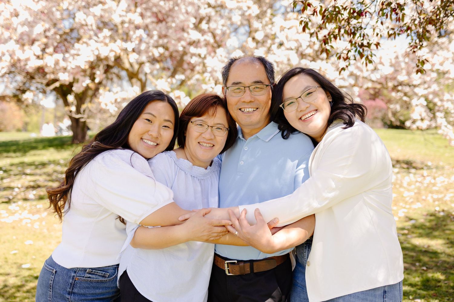 A family poses together outdoors during cherry blossom season with pink flowers blooming in the background.