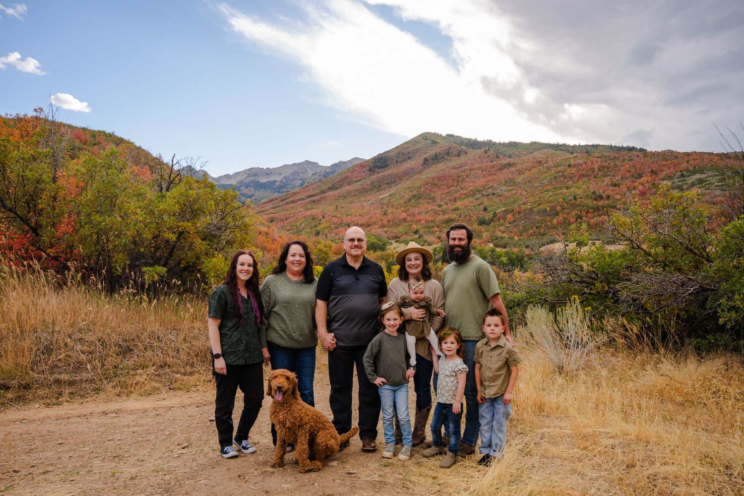 Extended family portrait outdoors in autumn mountains with golden foliage and golden retriever.
