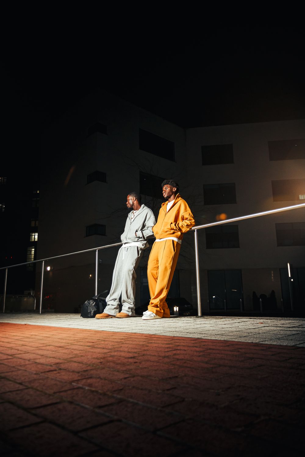 Two figures in white and orange robes sit on steps at night, creating a dramatic contrast in the dark setting.