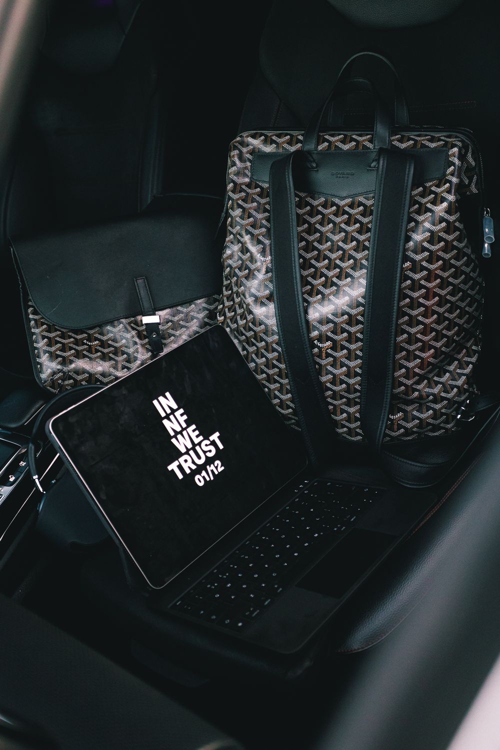 Luxury designer bags with monogram pattern arranged in car backseat with black tags visible in dim lighting.