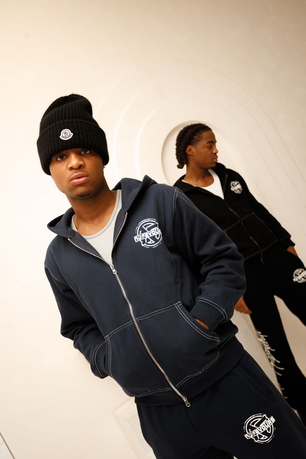 Four photos showing a person in a black zip-up hoodie with a circular logo patch posing against a white background.