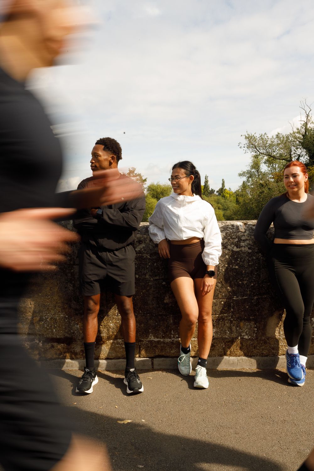 A sequence of people stretching and warming up together outdoors on a stone wall during an exercise session.